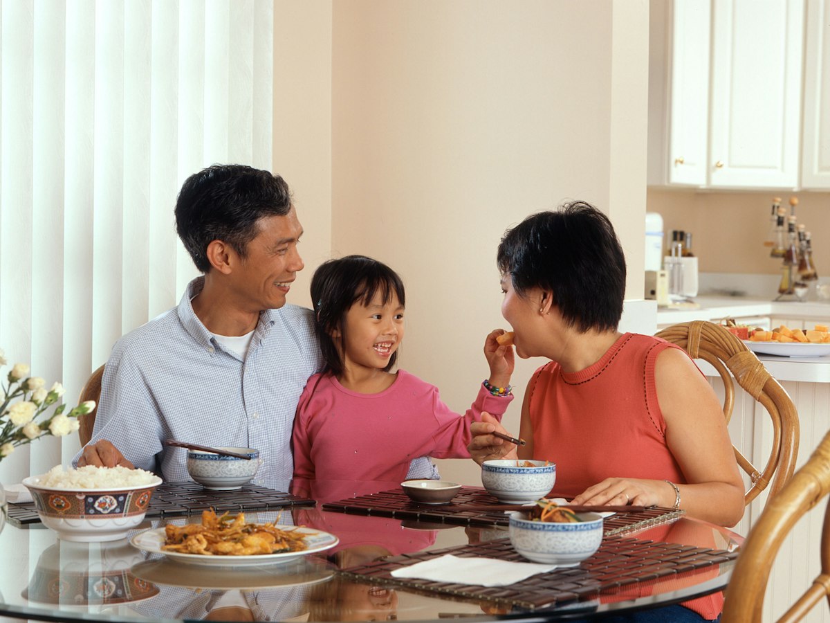 Parents and their young daughter laughing together over dinner at home