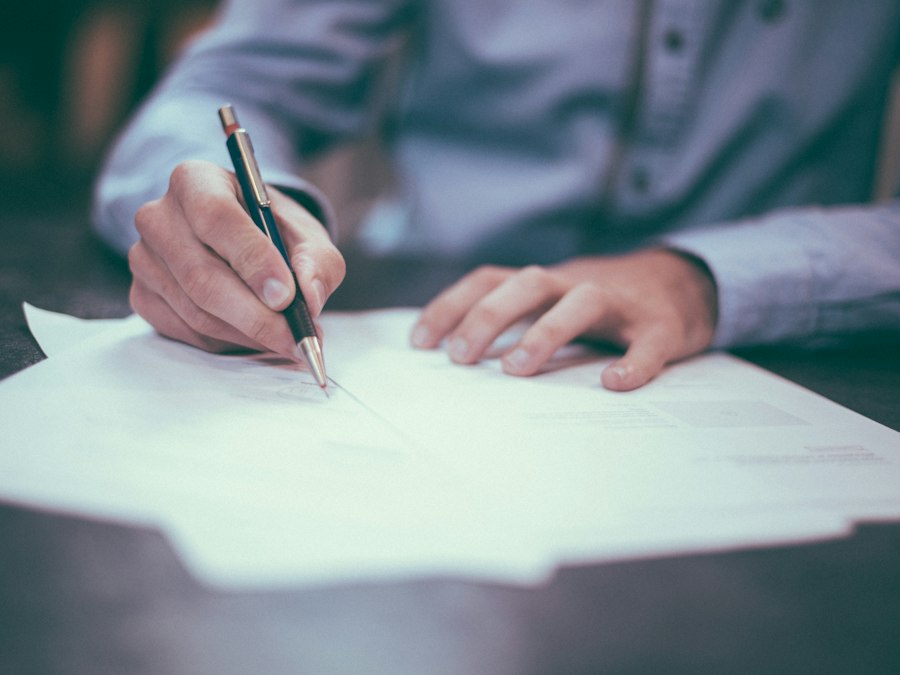 A hand signing a document with a pen
